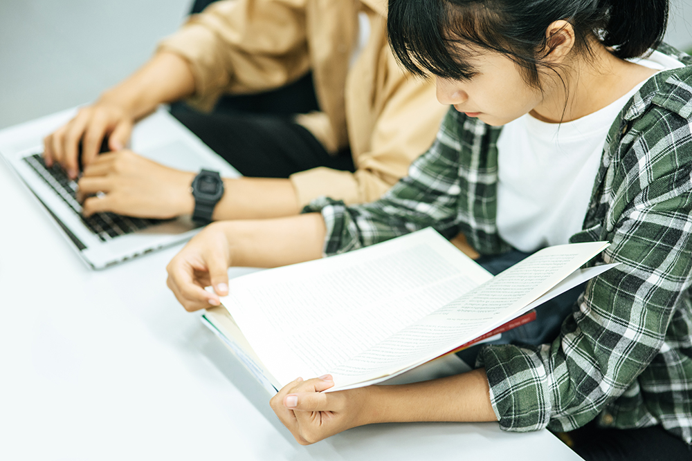 図書館で本やノートパソコンを使って調べものをする大人たち